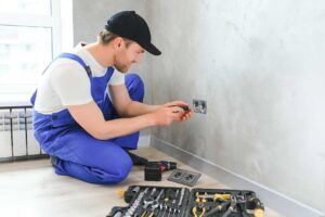 A person carefully replacing a light switch cover with a screwdriver, power clearly off, in a typical residential hallway.